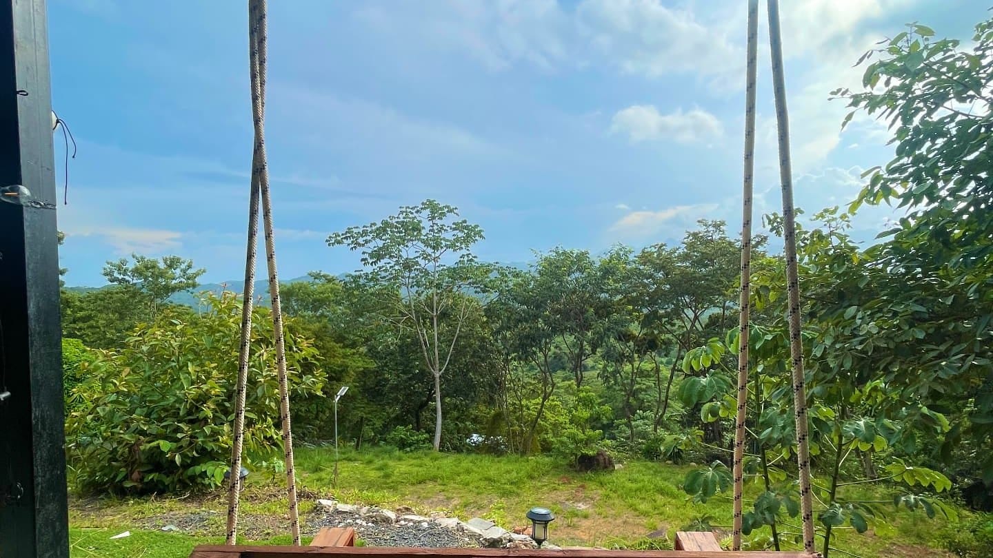 Columpio de madera con cuerdas frente a un valle verde y montañas bajo un cielo con nubes